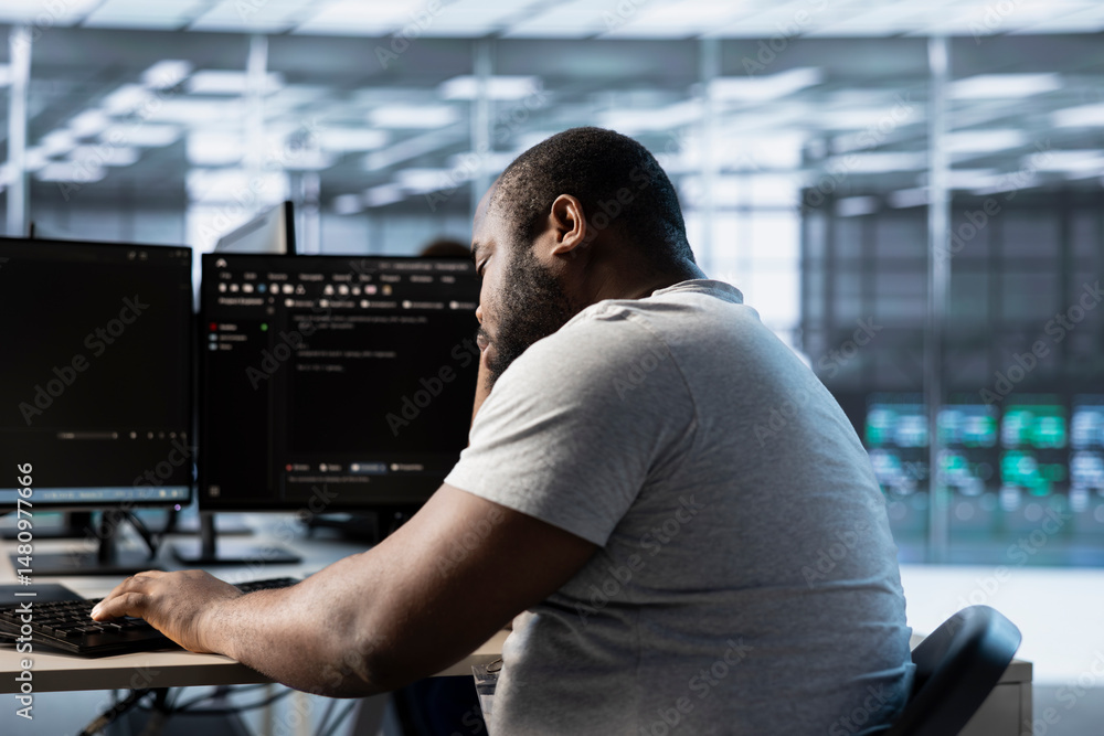 Poster fatigued engineer falling asleep while typing on computer in server hub, monitoring data center ener