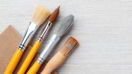 Fototapeta premium Art brushes resting on a light wood surface beside a paper notepad