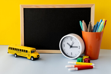 Back to school concept with blackboard colorful markers yellow school bus plastic dice modern clock...