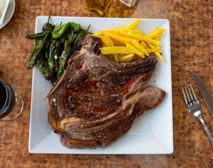 Grilled beef chop on the bone, served with a vegetable side dish of fried potatoes and green padron peppers