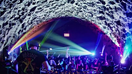 Wide-angle shot of a vibrant underground club scene with green lighting, a DJ, and dancing crowd, capturing a lively party video atmosphere.