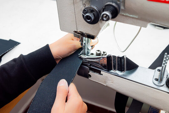 Close-up of a person sewing heavy fabric on an industrial sewing machine. The needle, presser foot, and hands are shown working on a piece of textile in a workshop. Shoe sewing machine, cylindrical.