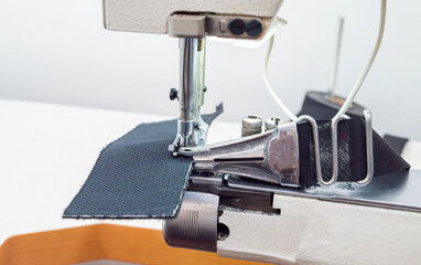 Close-up of a person sewing heavy fabric on an industrial sewing machine. The needle, presser foot, and hands are shown working on a piece of textile in a workshop. Shoe sewing machine, cylindrical.