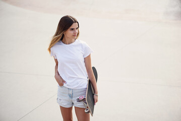 Young pretty girl in a white t-shirt and denim shorts holding skateboard.