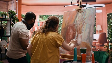 Team of painters collaborating on a rustic masterpiece in art studio, using creative painting techniques with brushes and watercolor paint. Applying multicolored dye on canvas. Camera B.