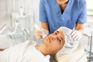 Experienced female cosmetic doctor carefully performs procedure on her male patient using...