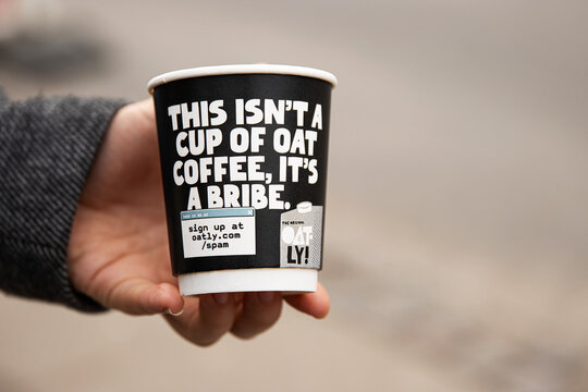 Copenhagen, Denmark, February 22nd, 202. Womans hand holding an Oatly, branded coffee cup in an urban setting. The black and white cup with the marketing slogan
