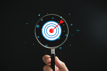 A magnifier glass highlights target board for focused business objectives, against a background...