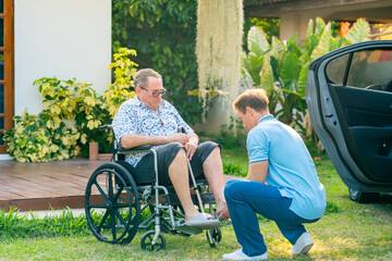 Male caregiver or taxi driver helping senior man patient on wheelchair get in the car go to...