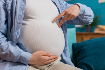Close-up shot of unrecognizable young pregnant woman walks her fingers over her large belly sitting...