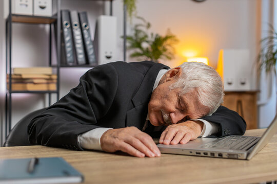 Bored sleepy senior businessman working on laptop computer, leaning on hand at home office desk. Exhausted tired grandfather freelancer workaholic guy falling asleep. Employment, occupation, workless