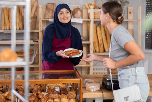 Female bakery seller in traditional islamic clothing offers to buy fresh baked goods to a european girl
