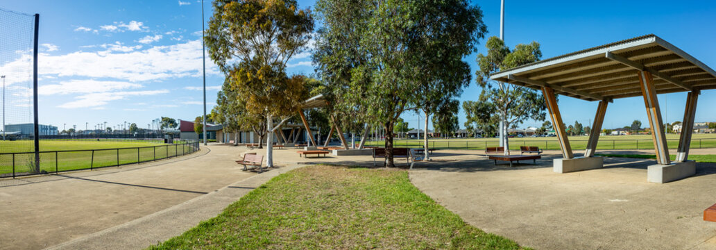 A public recreational space or a local sports reserve in suburban Melbourne, Australia, featuring modern shade structures, open seating benches, and green sports fields. 
