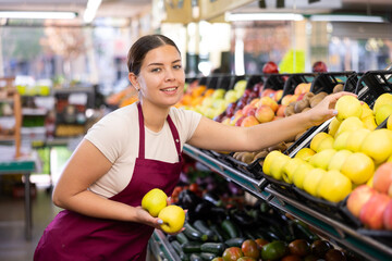 Young woman seller in uniform sells apples in grocery store