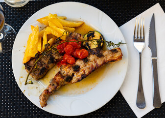 Spanish cuisine. Delicious grilled beef ribs with a side dish of fresh tomatoes and fried potatoes