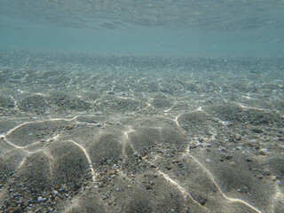 Dark blue ocean surface seen from underwater. Abstract waves underwater and rays of sunlight shining through, Sun light rays undersea deep, Underwater background with sea bottom, Mediterranean sea.