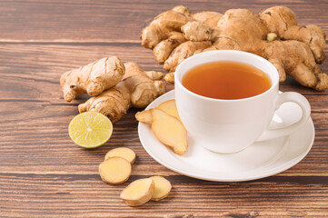 Cup of hot ginger tea with ginger root and slice on wooden table background.