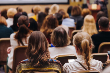 Female audience at the symposyum meeting, participants attendees in conference room hall listens to lecturer, group of women on a medical congress together listen to speaker on a stage at master-class