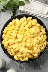 Delicious pasta with cheese sauce in bowl and parsley on grey table, flat lay