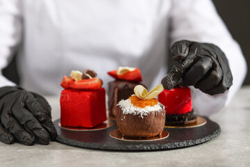 Confectioner decorating tasty dessert at light grey table in kitchen, closeup