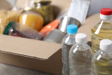 Bottles of water and different food products in box on table, closeup