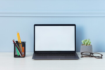 Naklejka na ściany i meble Laptop, stationery, glasses and floral decor on office table near light wall