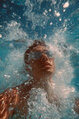 A person enjoys a refreshing swim, submerged in the water, with sunglasses on and water splashing around.