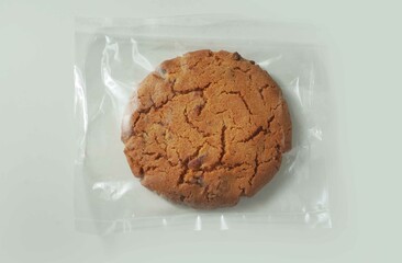 Cracked and brown cookie wrapped in plastic pillow pack on a white background