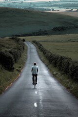 Obraz premium A lone cyclist rides along a peaceful country road with rolling hills in the distance.