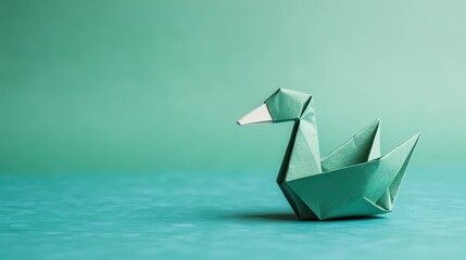 A green origami swan sits on a matching teal surface with a soft, minimal background.