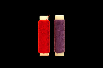 Red spool and Purple spool of sewing thread isolated on black background 