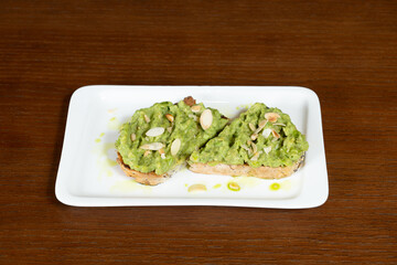 Avocado bruschetta with cream in a white plate on a restaurant table