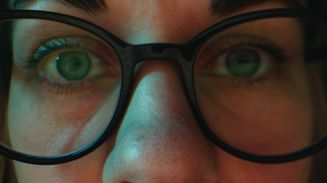 Close up of tired woman working at night on laptop, girl in eye glasses with reflections overworking busy, using computer in dark office
