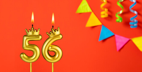 Number 56 birthday candle on an orange background with pennants