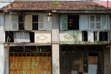 Abandoned colonial era heritage shophouse facade with weathered wood, old paint, and broker window...