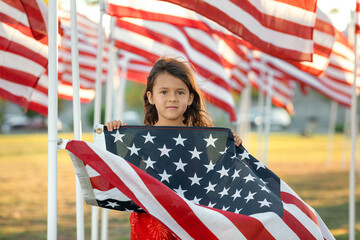 Patriotic holiday girl holding an American flag on a Memorial Day and looking at camera, Proud USA kids and 4th of July concept