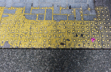 Old yellow blocks of tactile paving for blind handicap. Aged tactile pavement for the visually impaired close up background. Texture of gray square paving tile with Braille blocks in the street.
