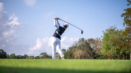 Professional female golfer lush green golf course, mid-swing after hitting a shot through after driving the ball down the fairway trees and distant sand bunkers, typical of a competitive setting.  