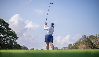 Professional female golfer lush green golf course, mid-swing after hitting a shot through after driving the ball down the fairway trees and distant sand bunkers, typical of a competitive setting.  