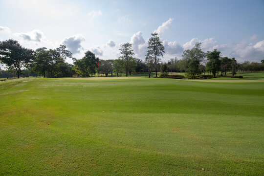 Golf course under a clear blue sky with scattered cloud green fairway is bordered by clusters of trees, offering a tranquil and scenic view for tournament preparation or early play..