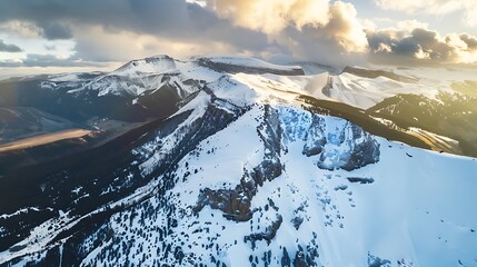 Obraz premium Snow Covered Mountain Range Under Cloudy Sky with Golden Sunlight View