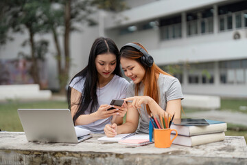 Diverse female students sharing a mobile device and studying together outdoors.