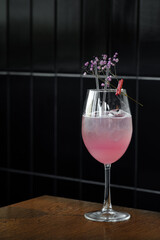 A pink gin and tonic cocktail in a clear glass, garnished with flowers and a red clothespin, set against dark tiles. This refreshing drink blends gin’s crispness with tonic’s fizz