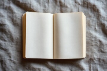 Open blank notebook with textured cream-colored pages lying on a soft, crumpled grey fabric surface suggesting calm and potential creativity