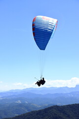 Paraglider flying over a mountain range. Outdoor adventure, scenic backdrop under a vivid blue sky
