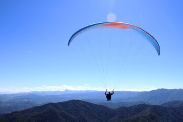 Paraglider flying over a mountain range. Outdoor adventure, scenic backdrop under a vivid blue sky