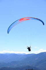 Paraglider flying over a mountain range. Outdoor adventure, scenic backdrop under a vivid blue sky