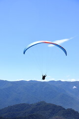 Paraglider flying over a mountain range. Outdoor adventure, scenic backdrop under a vivid blue sky