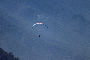 Paraglider flying over a lush forest landscape enveloped by mist. Outdoor adventure, scenic...