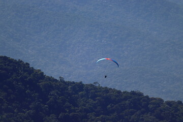 Paraglider flying over a lush forest landscape enveloped by mist. Outdoor adventure, scenic...